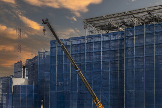 Construction site blue safety net crane building sunset sky urban development steel structure industrial architecture cityscape progress modern exterior scaffolding engineering equipment safety