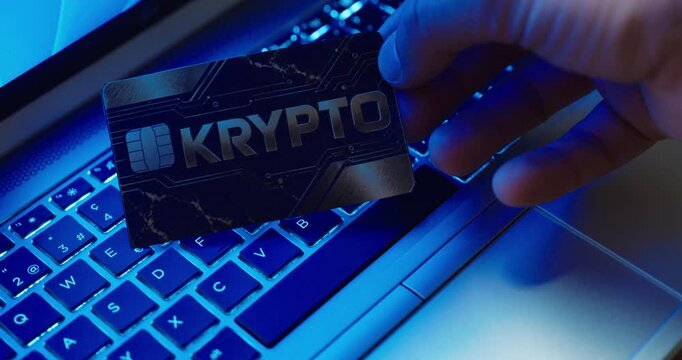 Close-up of a hand holding a crypto payment card over an illuminated laptop keyboard. Concept for cryptocurrency, online payments, blockchain, fintech and digital banking.