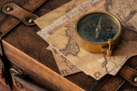 Old vintage maps and brass compass on top of a vintage leather luggage case. Vintage travel background backdrop concept.