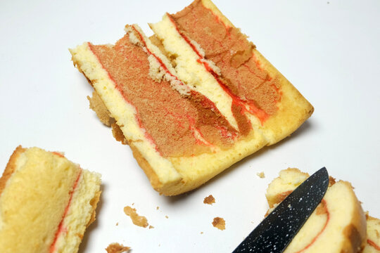 An overhead view of sliced swiss roll cakes and cake crumbs spread on a white surface next to a black knife blade