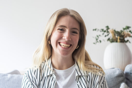 Happy young blonde woman smiling brightly and looking at camera during a casual video call at home, radiating positive emotions and friendly connection