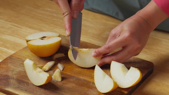 Person using a kitchen knife to remove the core and seeds from a sliced Asian pear