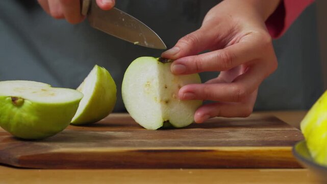 Slicing a Fresh Crystal Guava or Psidium Guajava into Thin Wedges on a Wooden Cutting Board