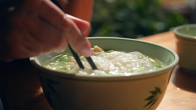 Pho Soup in Vetnam. Young Woman enjoys authentic vietnamese pho soup, using chopsticks. The traditional street food dish