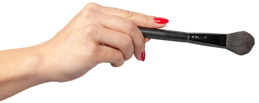 Hand holding a makeup brush ready for application in a bright setting