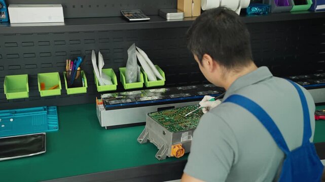 Auto technician servicing an electric car battery pack on a workbench in a garage, with vehicles and coworkers in the background during diagnostics and repair.