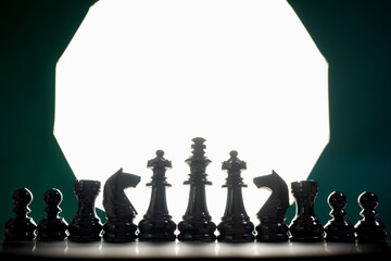 Row of Black Chess Pieces Silhouetted Against Bright Light © Evolusix