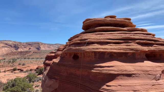Layered desert rock formation rises above arid hills and shrubs beneath a clear blue sky. Nature documentaries, geology education, and desert tourism promotion.