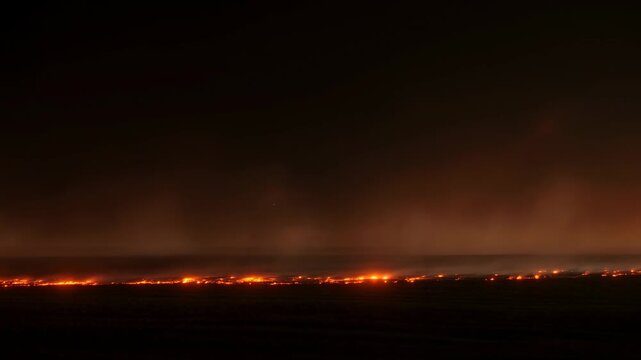 Wildfire spreads across an open landscape beneath a dense smoke plume at night. Wildfire news coverage, disaster preparedness campaigns, and emergency management presentations.
