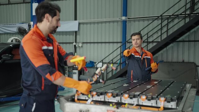 Mechanic man inspecting an electric vehicle battery with a digital tablet in a clean service bay environment