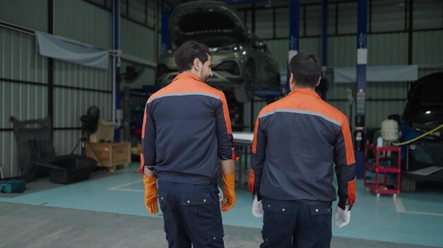 Manager Checks Diagnostics Results on a Tablet Computer and Explains a Vehicle Breakdown to a Handsome Mechanic. Car Service Employees Talk while Walking in a Garage. Modern Clean Workshop.