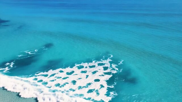 Turquoise waves roll toward a white sandy beach lined with palm trees during an aerial coastal view of a tropical island shoreline
