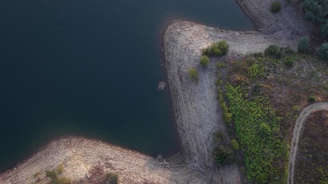 Drone shot captures parched riverbanks, low water levels, and exposed land during drought in Portugal, illustrating climate change effects with striking natural contrast.