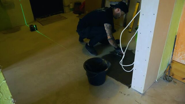 Construction worker carefully laying new ceramic floor tiles on adhesive during a home renovation project. Accurate installation process using a laser level for precision home improvement