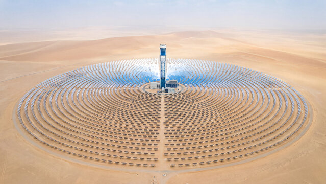 Aerial drone view of solar thermal power station in desert, circular heliostat field around central tower, concentrated solar energy plant for clean renewable electricity