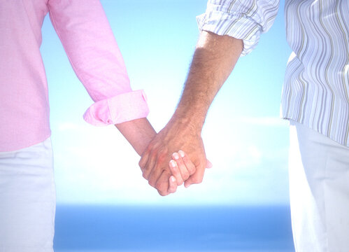 Midsection of couple holding hands with sea in background