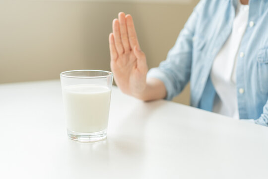 Allergy asian young woman, girl hand in deny, no or push out to avoid for drink milk at home, unhappy and bad stomach ache. Lactose intolerance and dairy food, health problem, belly suffer concept.