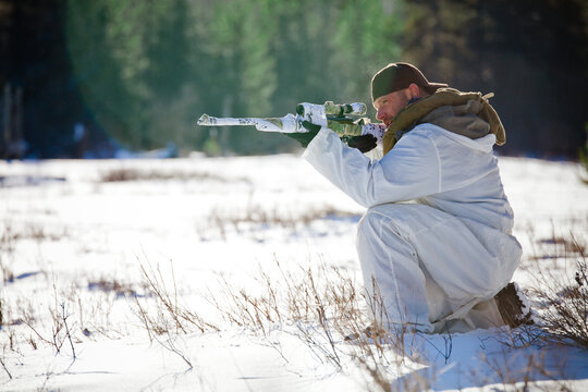 A manwearing  a coldweather camouflage outfit aims a rifel while