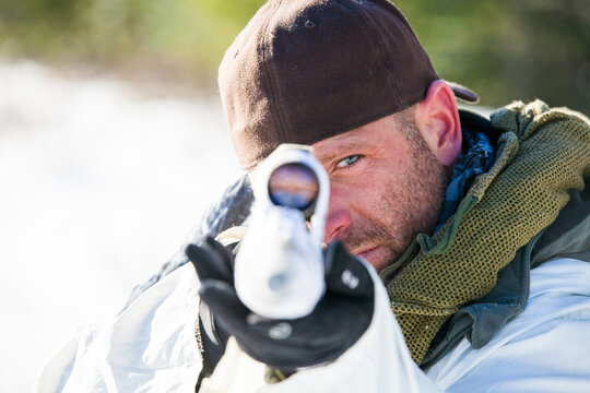 Man with blue eyes aiming a rifle with a scope at you