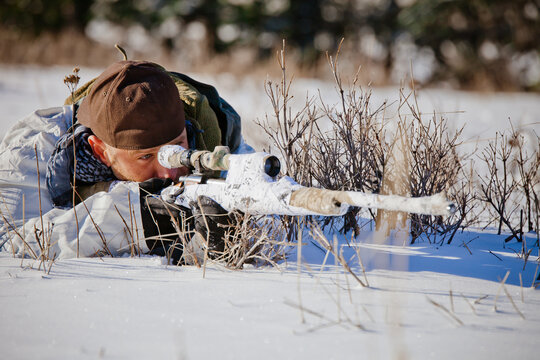 A hunter wearing  a coldweather camouflage outfit aims a rifel at his