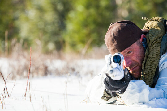 Man aiming a sniper rifle at the camera in snow