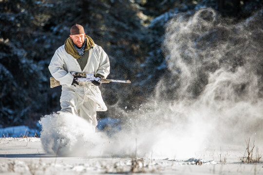 Man in winter camouflage runs through deep snow with a rifle