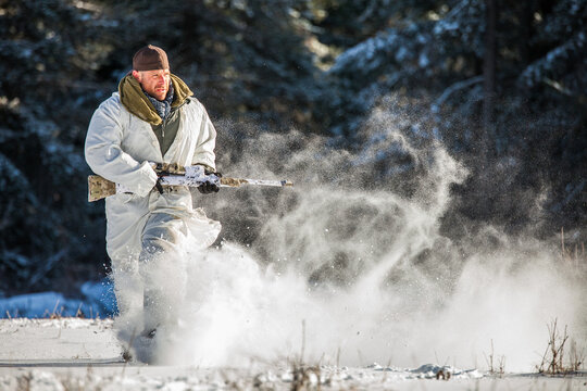 Man in white winter camouflage running through deep snow with rifle