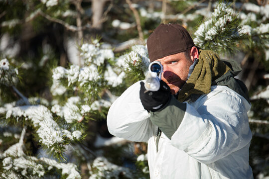 Hunter in snow camouflage aims his rifle