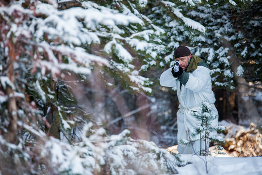 Man in white camouflage aiming rifle in snowy forest