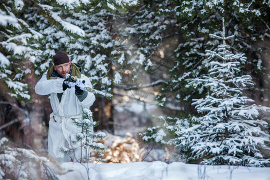 Man in winter camouflage aims a rifle in a snowy forest