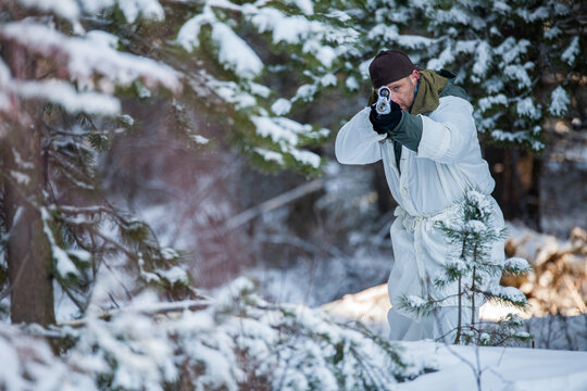 Man in winter camouflage aims handgun in snowy forest