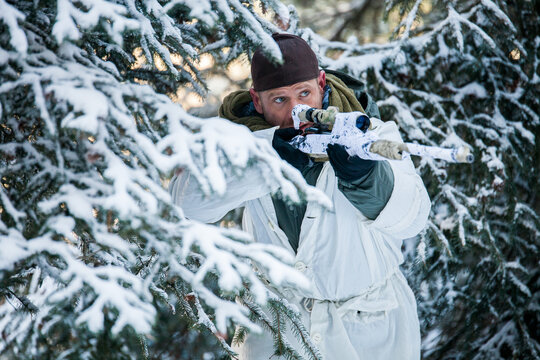 Sniper in winter camouflage aims rifle in snowy forest