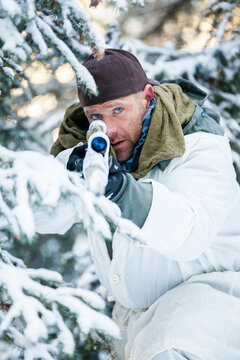 Hunter in winter camouflage aims rifle in snowy forest