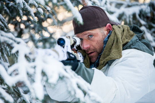 Man with blue eyes aims a sniper rifle in snow