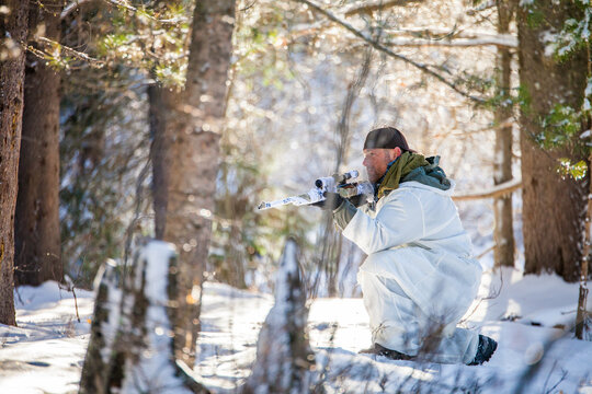Armed hunter wearing winter camouflage hidden in forest
