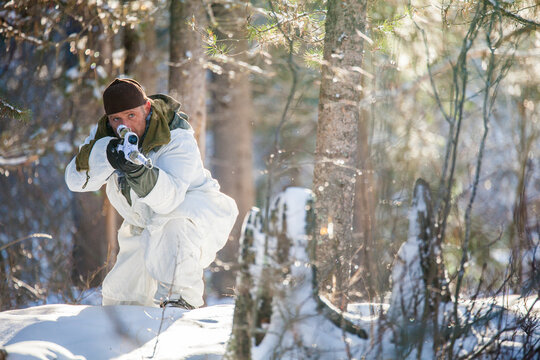 Hunter in snow camouflage aiming rifle in a winter forest