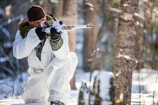 Man in white winter camouflage aiming sniper rifle