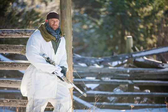Man in white snow camouflage holding a sniper rifle