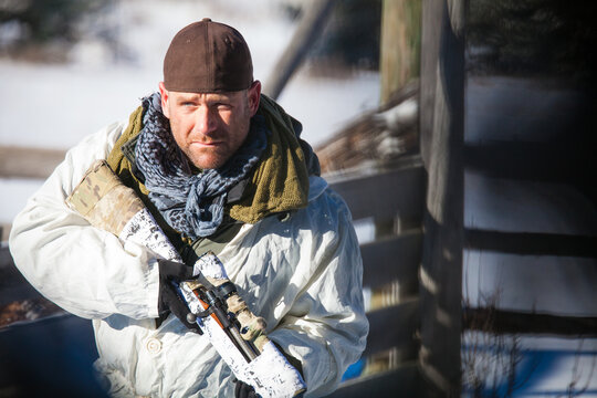Man in winter camouflage holds rifle in snow