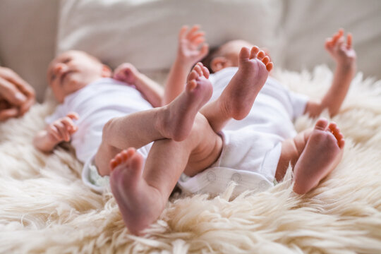 Newborn twins kick their feet in the air with lying on sheepskin