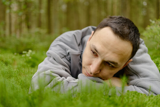 Caucasian young adult man lying on green moss in forest resting head on hands outdoors. Concept representing mental health, mindfulness, eco therapy and wellness campaign