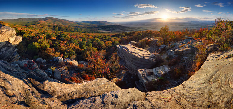 Panorama of sunset mountain landscape with forest and rocks.