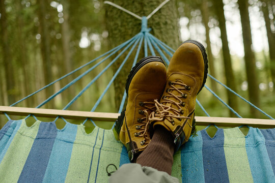 Hiker resting legs in hammock hanging between trees in forest, representing ecotourism and relaxation. Perfect for travel marketing and outdoor recreation campaigns
