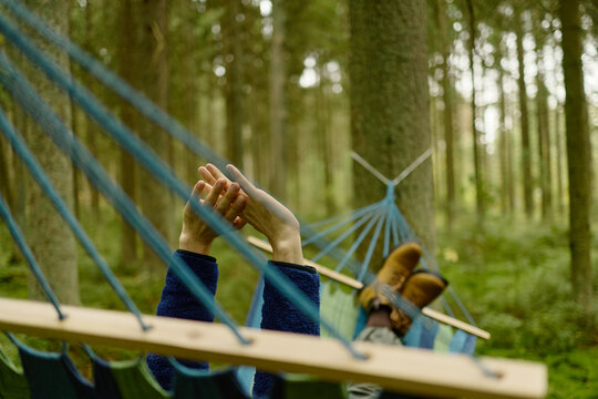 Caucasian young adult relaxing in hammock among forest trees, stretching hands upwards. Concept of ecotourism and mental wellbeing, perfect for outdoor travel campaigns, POV shot