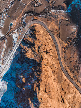 Top down aerial view of asphalt mountain road winding around towering steep cliffs