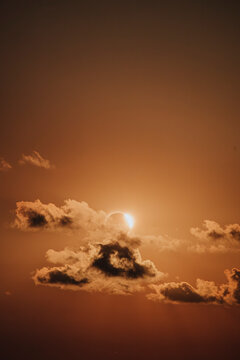 Partial solar eclipse shining through dark cloud in an orange sky