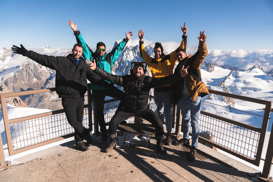 Happy friends with hands raised at viewpoint at Aiguille Du Midi, Mont Blanc, Chamonix, France
