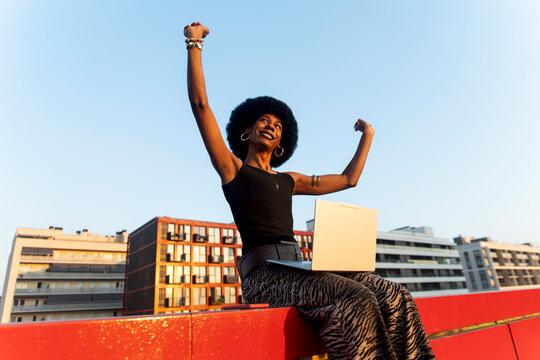 Happy queer digital nomad celebrates success with laptop outside