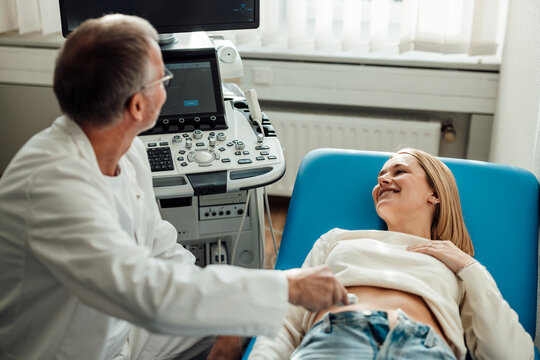 Doctor performing ultrasound scan on smiling pregnant patient indoors