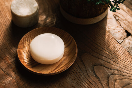 Natural white soap rests on a wooden dish in warm sunlight